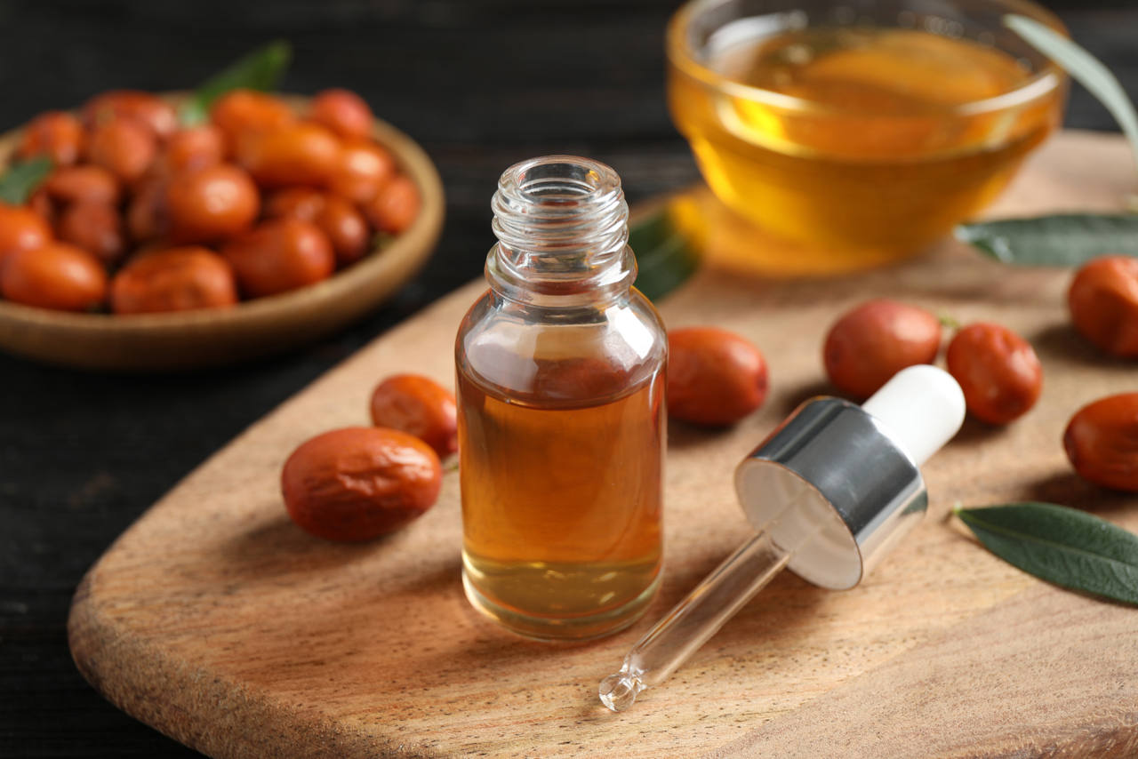 Glass bottle with jojoba oil and seeds on black wooden table